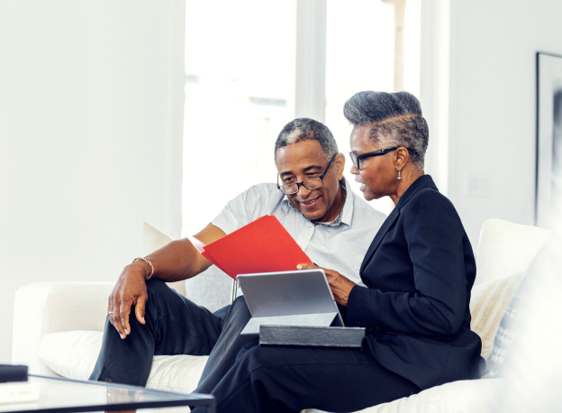 Female banker in black suit showing a red file to a male client while seated on a white couch