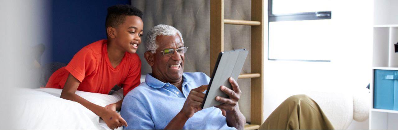 Grandpa sitting on couch holding a tablet with grandson looking over