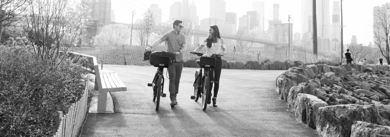 a man and woman walking their bikes through an urban park