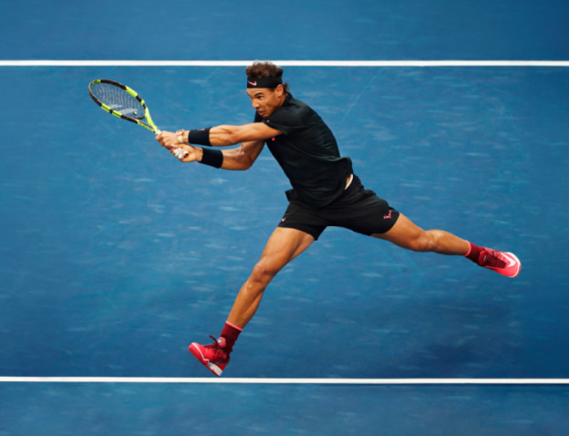 Rafael Nadal against blue background having hit the tennis ball energetically