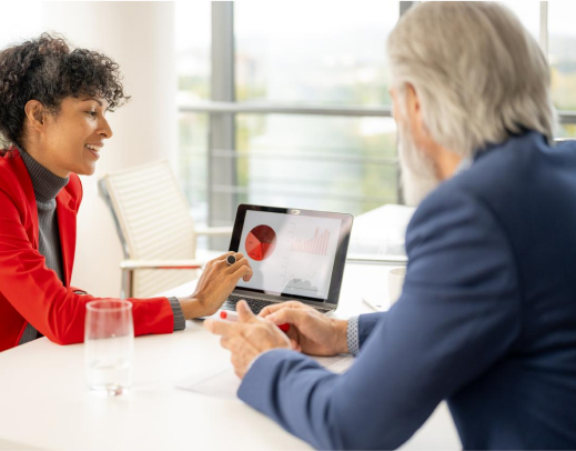 Woman showing a pie chart on a laptop to man in an office.