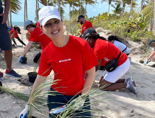 Woman in red Santander shirt helping clean up a beach after a storm