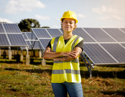 Woman in a yellow vest and hard hat standing in front of solar panels