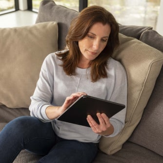 A woman sitting on a couch looking at the screen of a tablet.