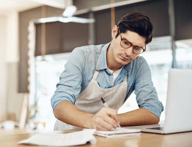 Man writing on a notepad next to an open laptop.