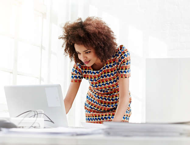 Woman standing at a desk, leaning over a laptop.