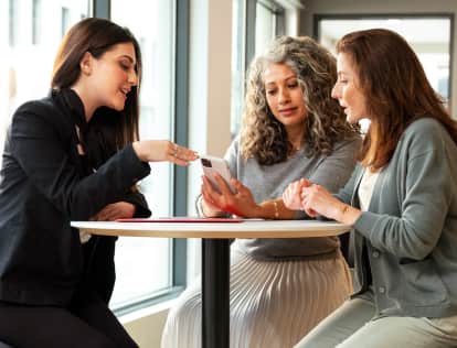 3 woman sitting at a table looking at a cell phone