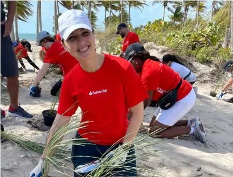 Woman in red Santander shirt helping clean up a beach after a storm