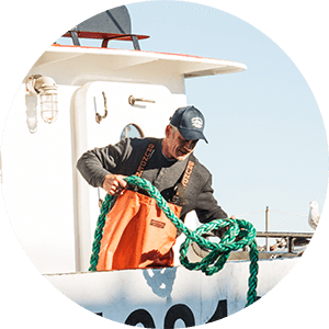 man pulling rope out of water on side of boat