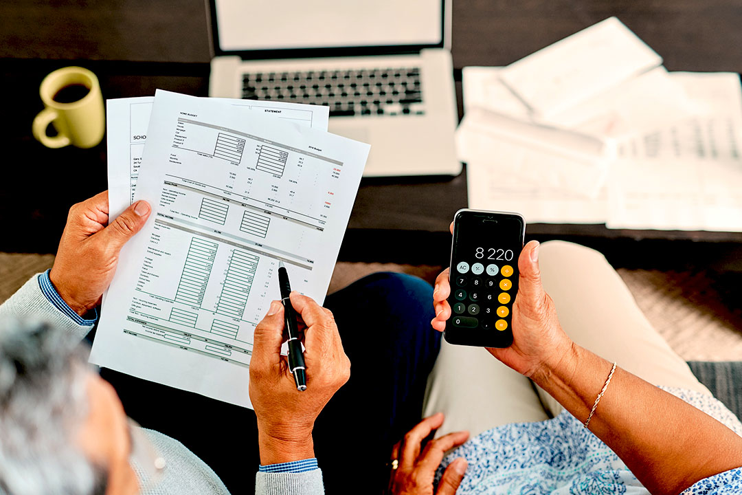 Overhead view of a couple looking at financial paperwork, using a calculator, in front of a computer.