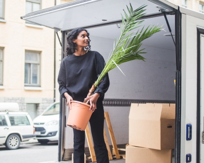 Young woman in the back of a moving truck filled with boxes carrying a plant out
