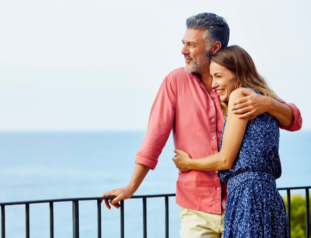 Happy couple hugging while overlooking the ocean on a balcony.