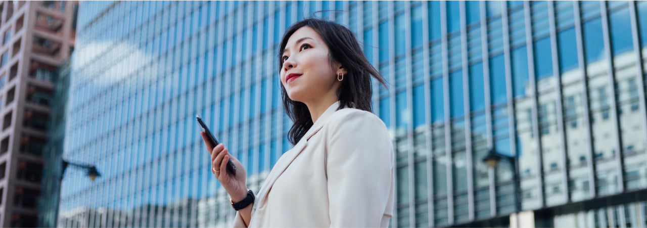 A business woman smiling in the city while holding her mobile phone.