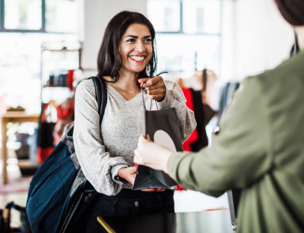 A woman taking her bag of her purchases from a sales associate.
