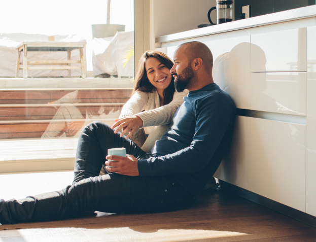a man and a woman sitting on their kitchen floor together smiling