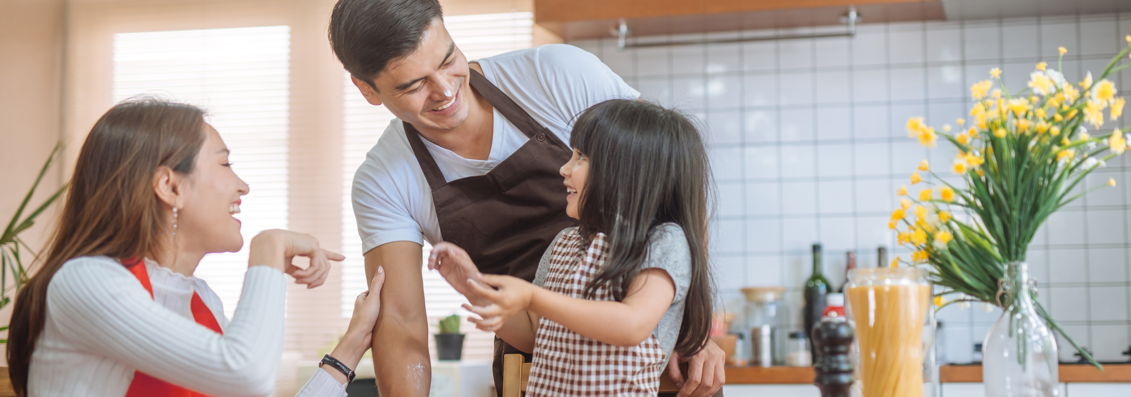 a mother and father happily cooking together in their kitchen with their young daughter