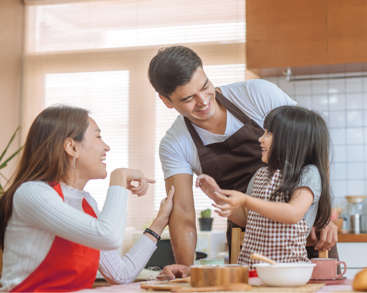 a mother and father happily cooking together in their kitchen with their young daughter