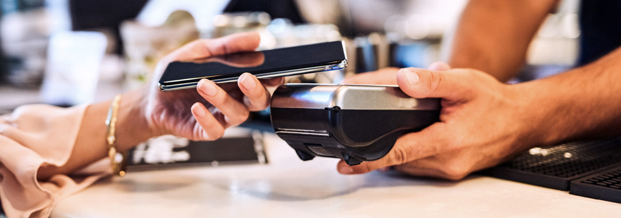 Close up of a customer paying with tap on her phone over a transaction machine.