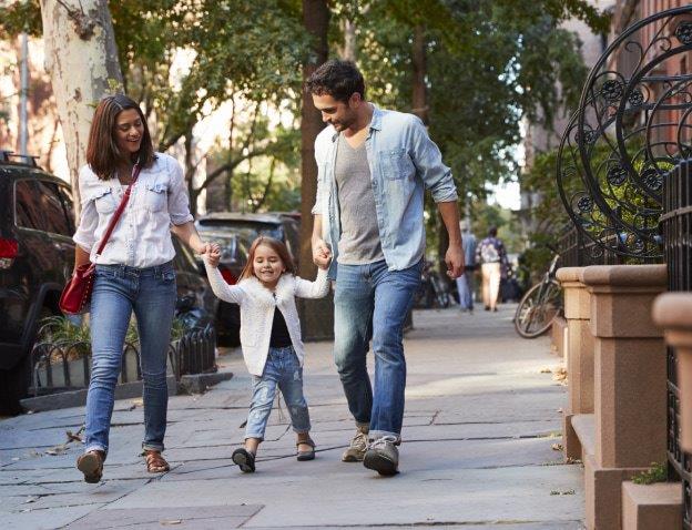 man and woman holding child's hands walking down a street