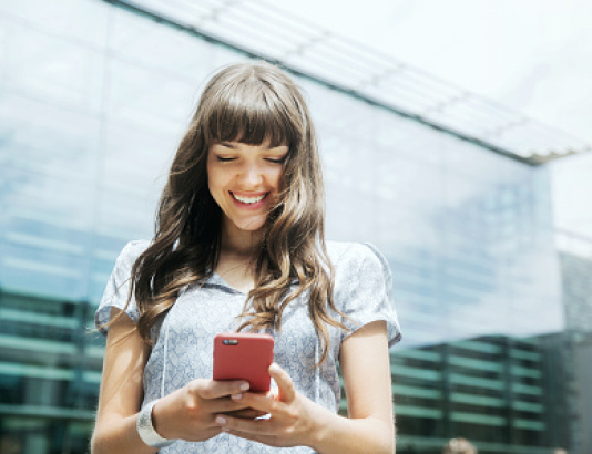 Woman smiling while looking down at her smart phone.