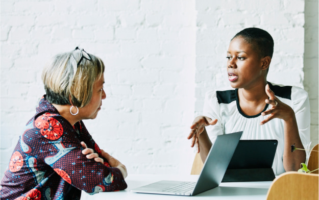 Two women with laptops talking at a table