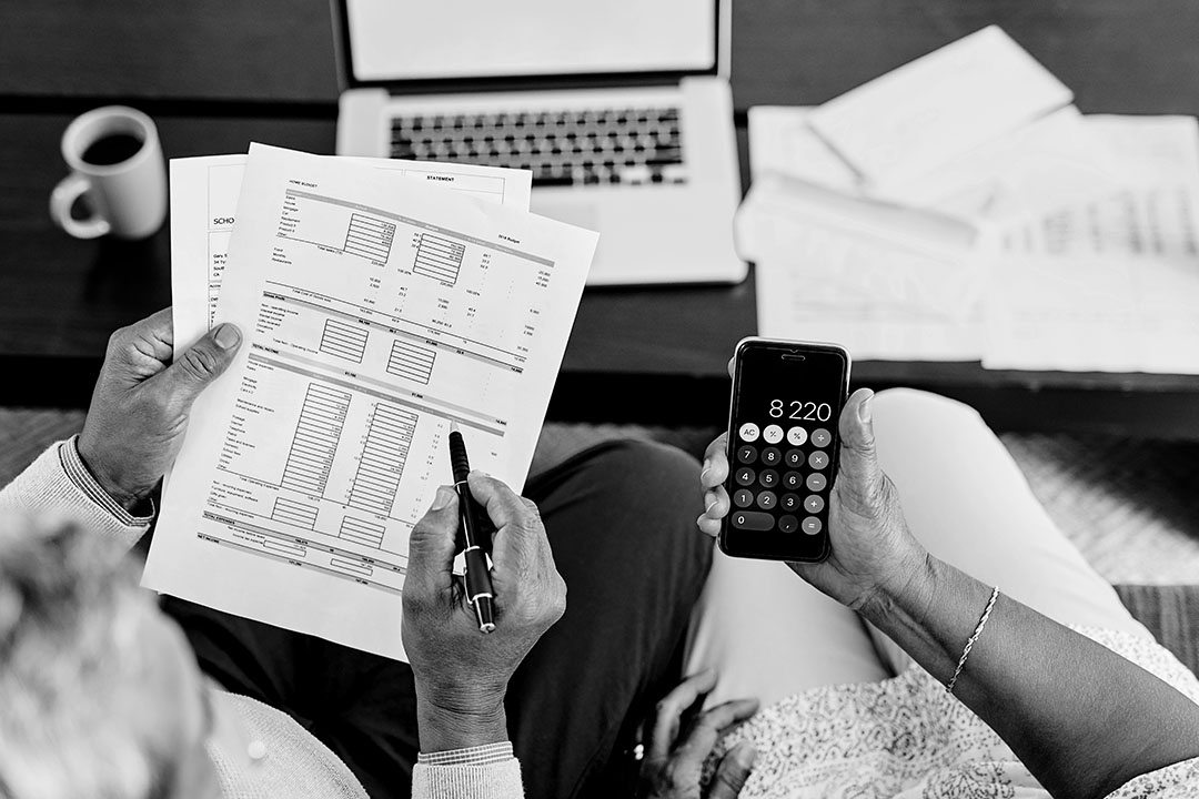 Overhead view of a couple looking at financial paperwork, using a calculator, in front of a computer.